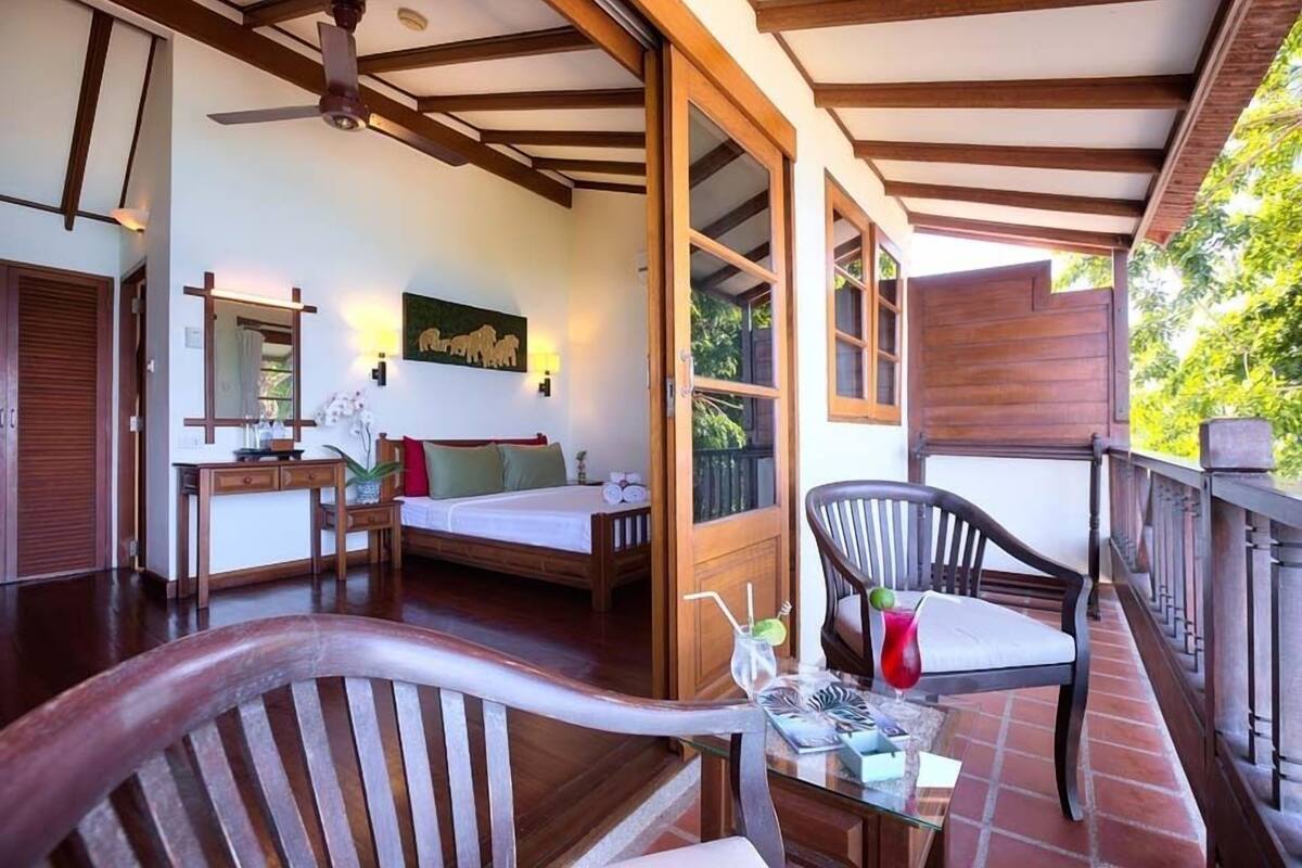 A room with a bed, a desk, a chair, and a balcony with a railing.