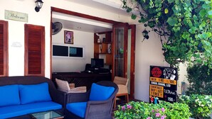 A cozy outdoor seating area with wicker furniture and a glass table, a bar area with a sign advertising drinks, and potted plants. - The Lodge (Koh Samui)