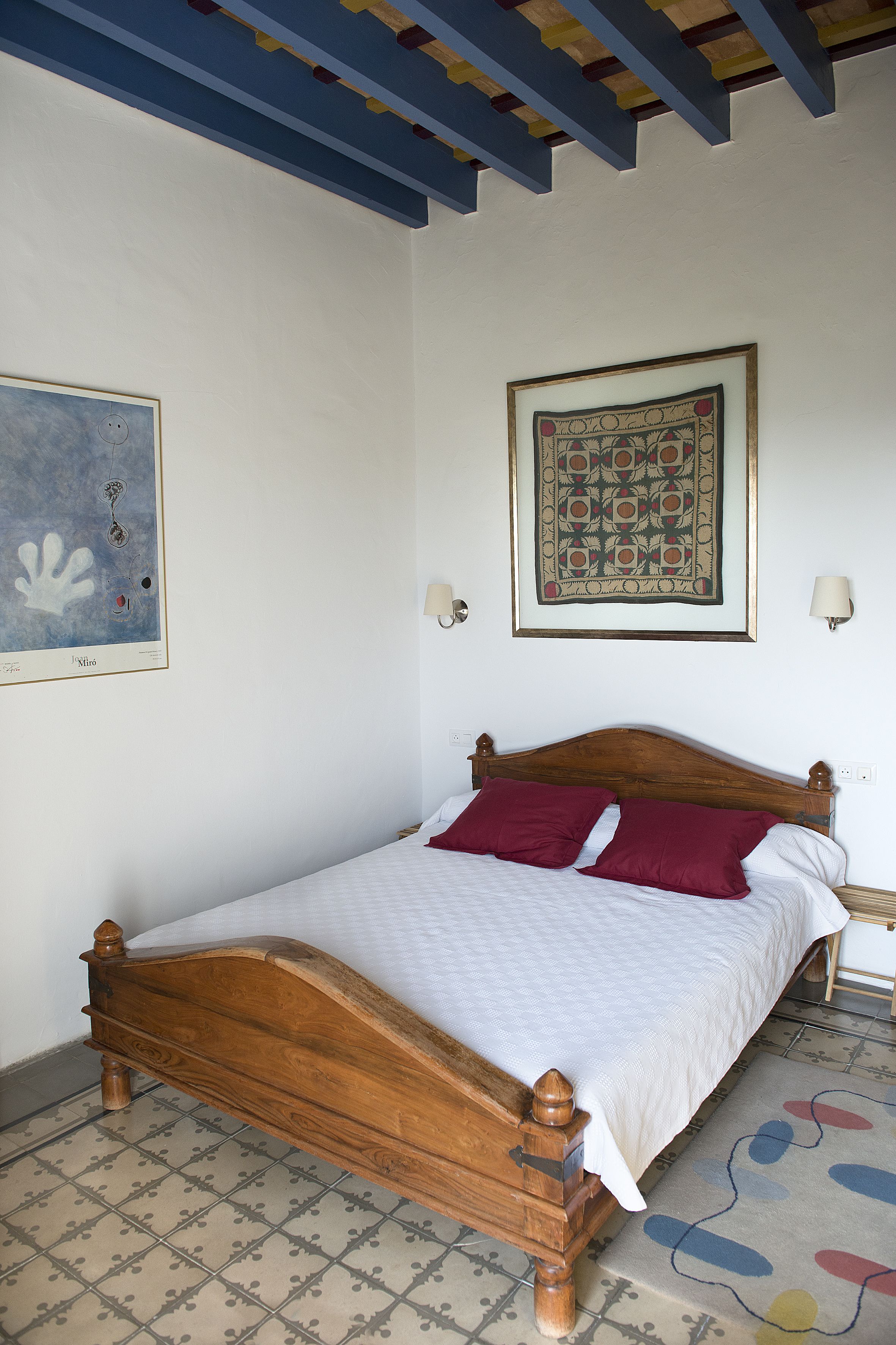 Un dormitorio con una cama de madera, ropa de cama blanca y una alfombra estampada.
