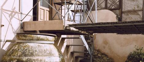 A courtyard with a large ceramic pot, a white chair, a small table, and a staircase leading to a building with a balcony.