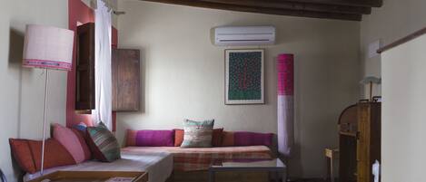 A cozy room with a sofa, a small table, a lamp, and an air conditioning unit on the wall.