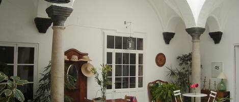 Un amplio patio con suelo a cuadros, una mesa de madera con sillas y varias plantas en macetas.
