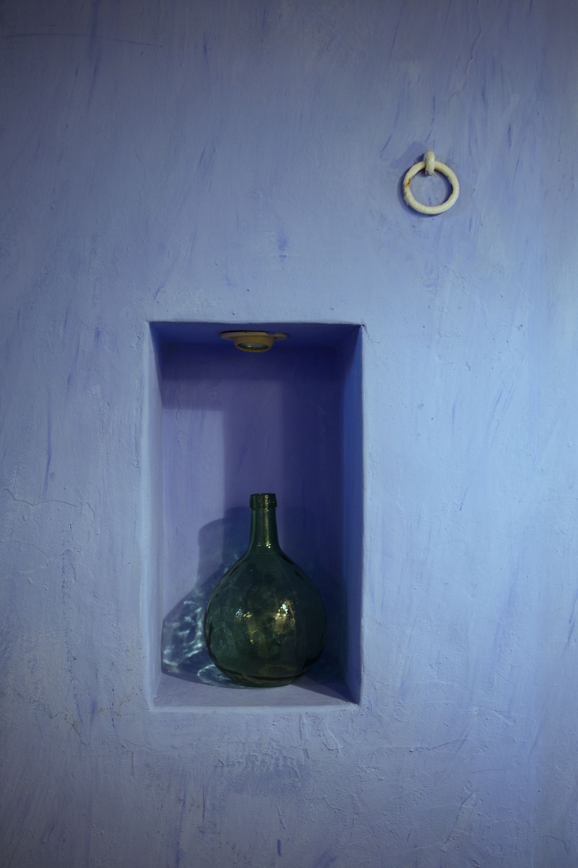 A green bottle in a blue-painted alcove with a metal ring on the wall.