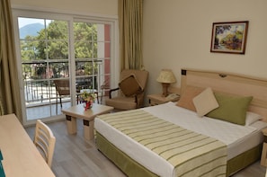 A hotel room with a bed, a chair, a table, and a balcony with a view of trees and mountains. - Grand Yazici Club Turban (Marmaris)