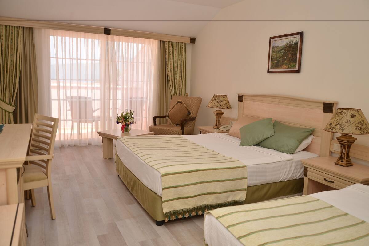 A hotel room with a bed, two bedside tables, a chair, a desk, and a window with curtains.