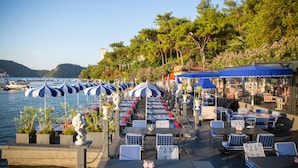 Restaurante à beira-mar com mesas ao ar livre, guarda-sóis e vista para a água.