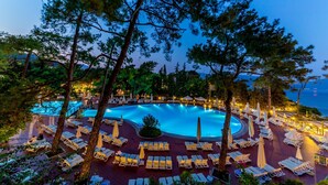 Uma piscina circular rodeada por espreguiçadeiras e guarda-sóis, com árvores emoldurando a paisagem.