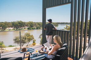 A balcony with a view of a river, a person reading a book, and another person standing by the railing. - The Frames (Paringa)