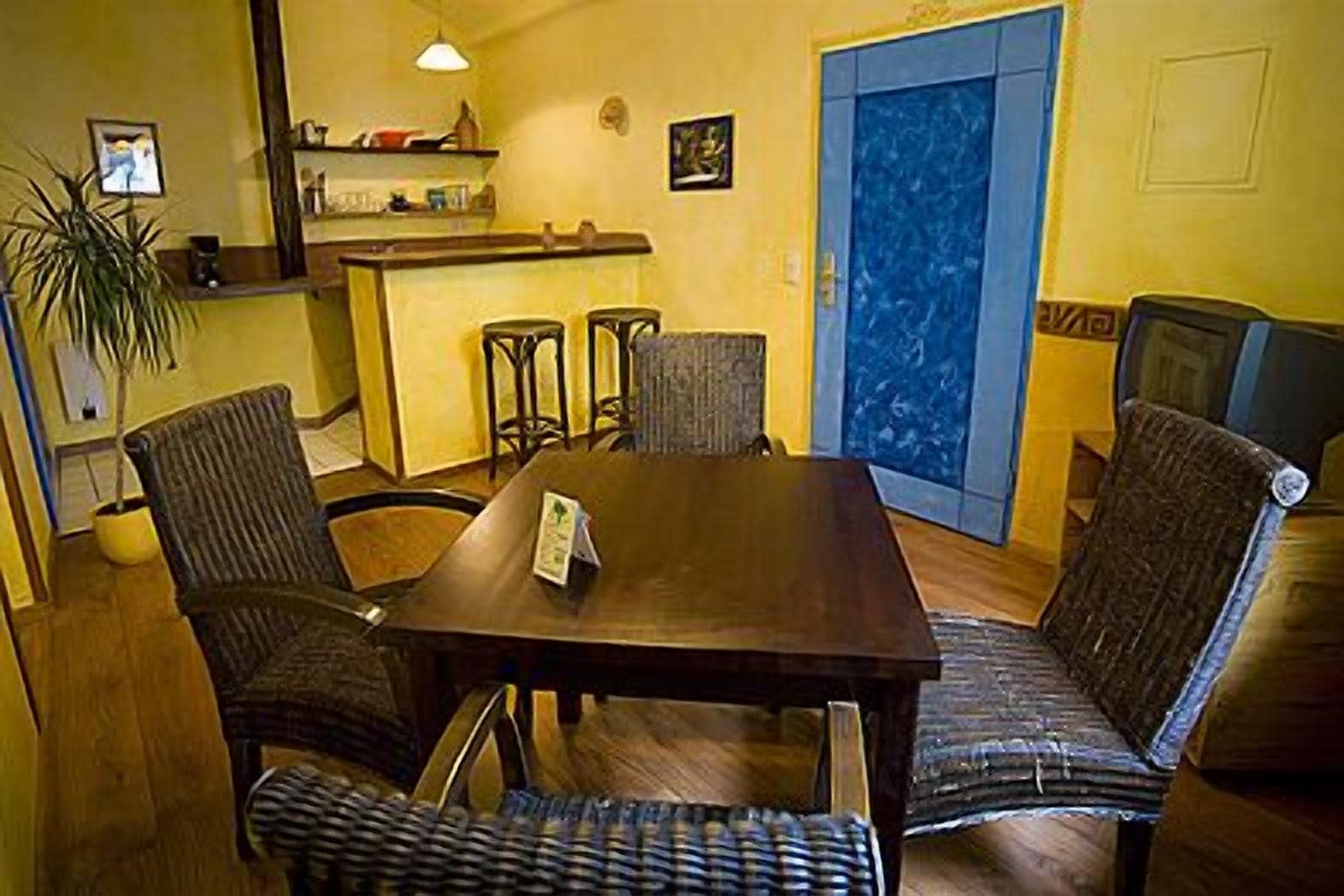 Un coin repas avec une table en bois et quatre chaises, une porte bleue et une plante.