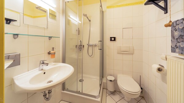 Un baño con ducha de vidrio, lavamanos con dispensador de jabón, inodoro y espejo.