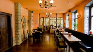 Een restaurantinterieur met houten tafels en stoelen, stenen zuilen en een kroonluchter.