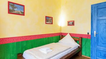Een kleine eenpersoonskamer met een houten bed, een groene en rode decoratieve rand en twee foto's in lijsten aan de muur.