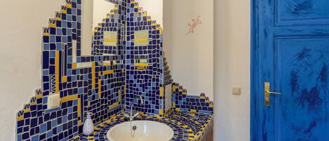 A bathroom with a blue door, a sink with a mirror above it, and a tiled wall.