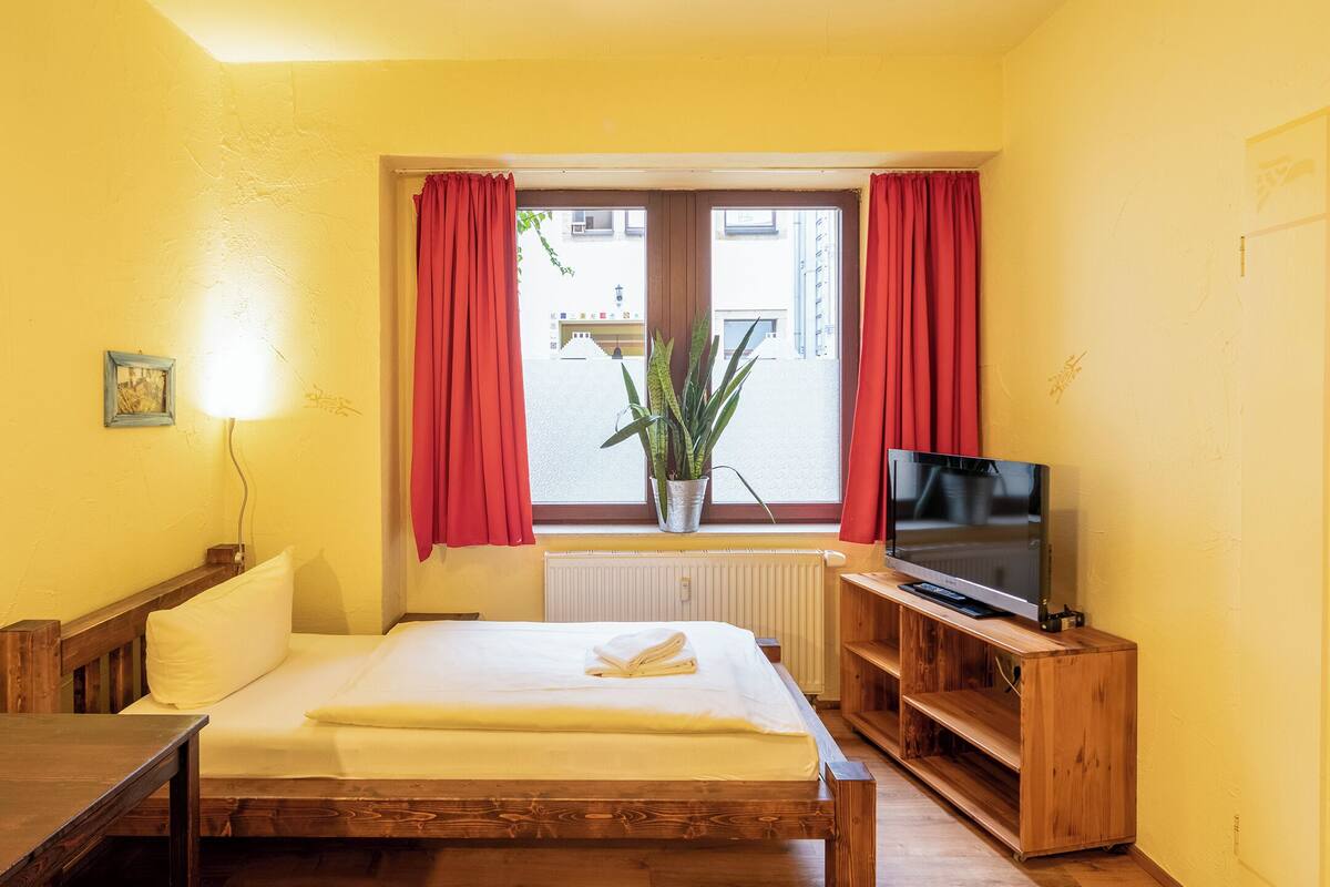 Een hotelkamer met een houten bed, een televisie, een bureau en een raam met rode gordijnen.