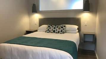 A neatly made bed with a green blanket, a headboard, and two bedside lamps.
