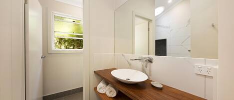 A modern bathroom with a wooden vanity, a white sink, and a large mirror.