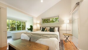 Un dormitorio moderno con una cama grande, un banco de madera, una ventana con vistas a zonas verdes y una mesita.
