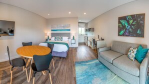 Una habitación de hotel moderna con una cama, un comedor con mesa y sillas, un sofá y una zona de cocina.