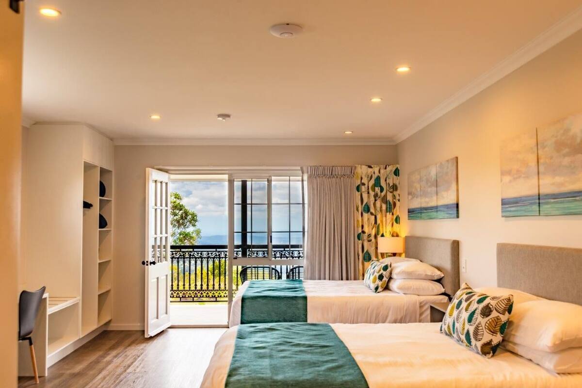 Habitación de hotel con dos camas, un balcón con vistas y un escritorio con una silla.