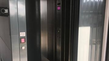 Liftinterieur met een digitaal scherm, noodknoppen en een waarschuwingsbord.