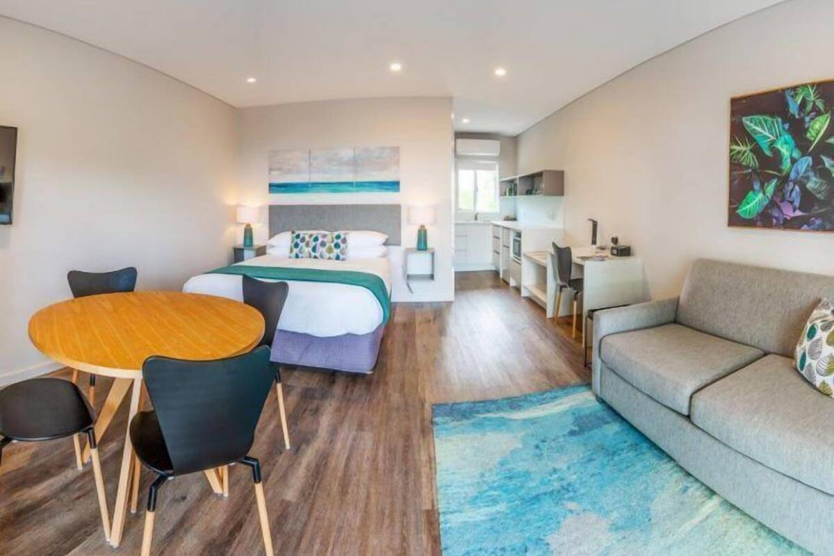 Una habitación de hotel moderna con una cama, una mesa de comedor con sillas, un sofá y una zona de cocina.