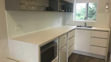 A kitchen with white cabinets, a built-in oven, a microwave, a sink, and a window with a view of greenery outside.