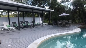 Zona de piscina con sillones de descanso y un espacio de estar techado.