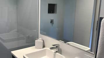 A modern bathroom with a glass-enclosed shower, a large mirror, and a white sink.