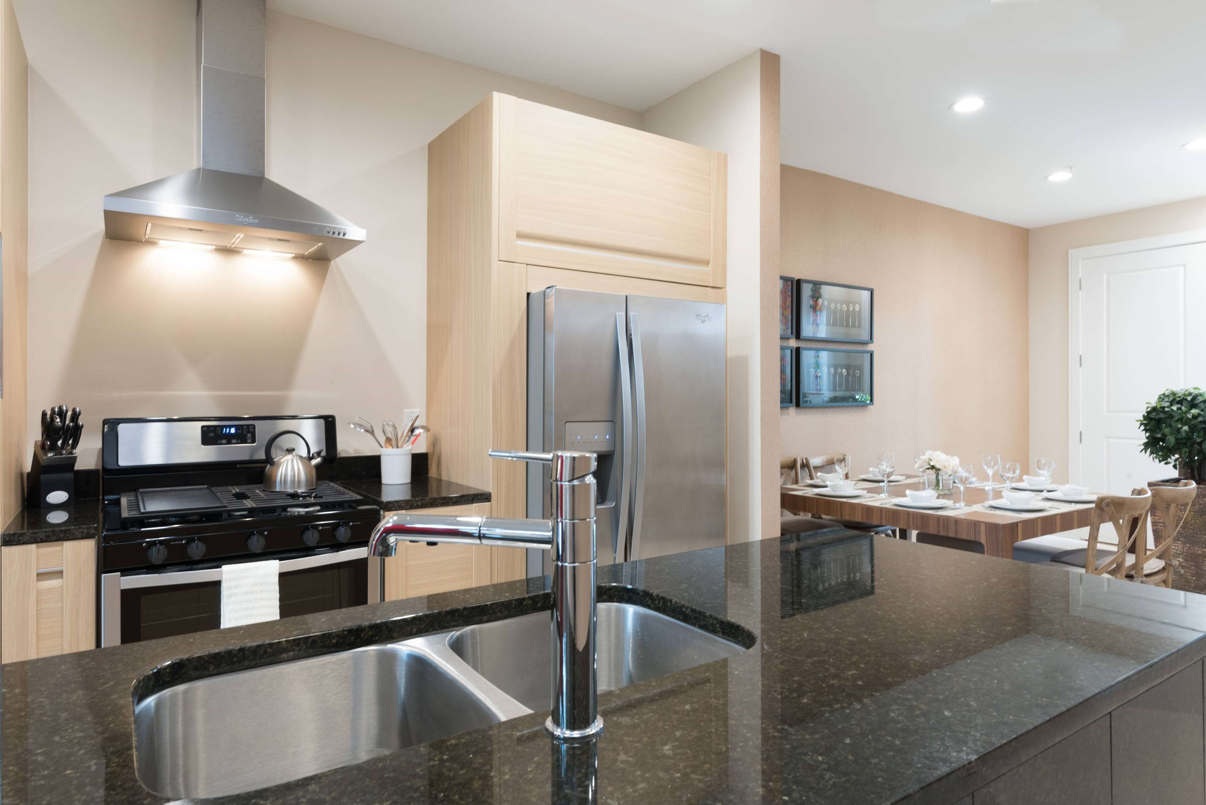 Cocina moderna con electrodomésticos de acero inoxidable, encimera de granito y comedor con mesa para cuatro.