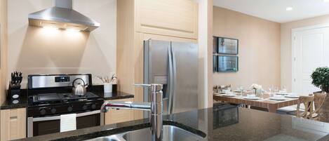 Cocina moderna con electrodomésticos de acero inoxidable, encimera de granito y comedor con mesa para cuatro.
