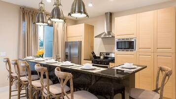 A modern kitchen with a central island, wooden cabinets, stainless steel appliances, and pendant lighting.