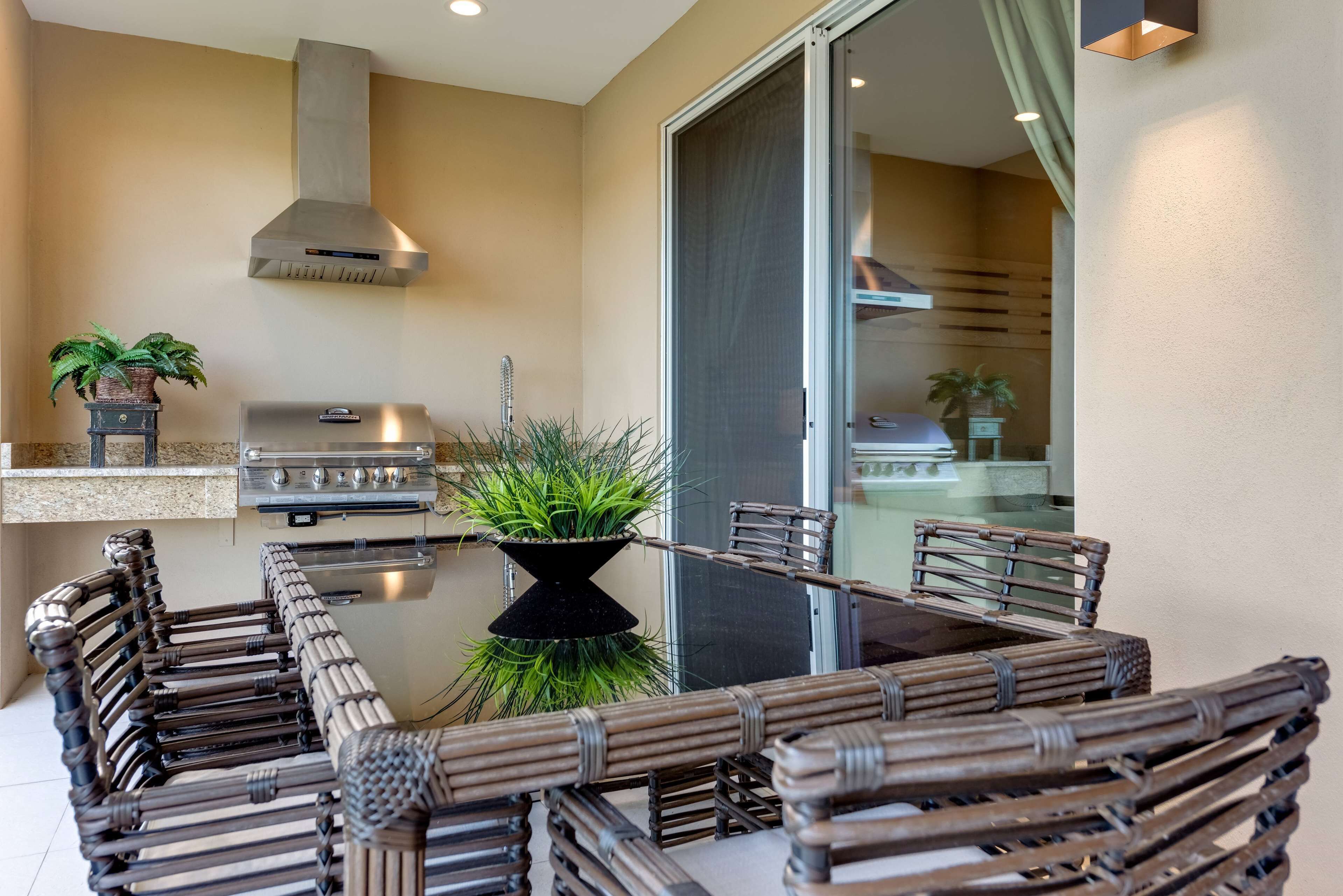 An outdoor patio with a grill, wicker furniture, and potted plants.