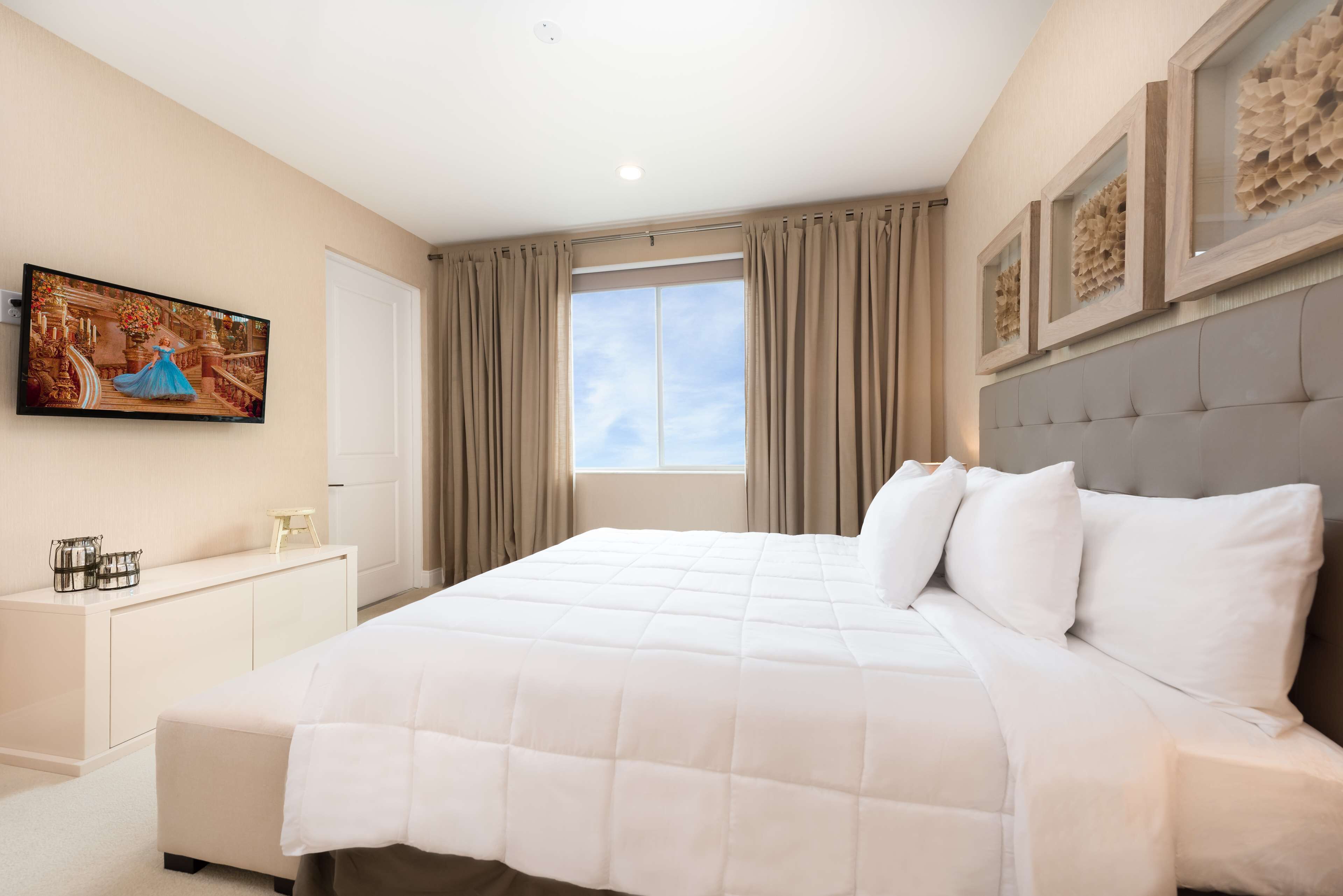 A modern hotel room with a large bed, a flat-screen TV mounted on the wall, a window with curtains, and a decorative wall panel.