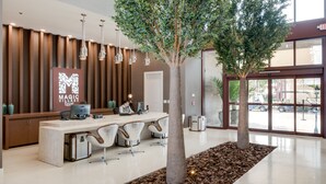 A reception area with a modern desk, chairs, a large tree, and a sign for Magic Village Resort. - Magic Village Yards, Trademark Collection by Wyndham (Kissimmee)