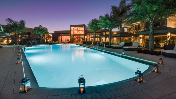 A swimming pool with a wooden deck, surrounded by palm trees and lounge chairs, with buildings in the background. - Magic Village Yards, Trademark Collection by Wyndham (Kissimmee)