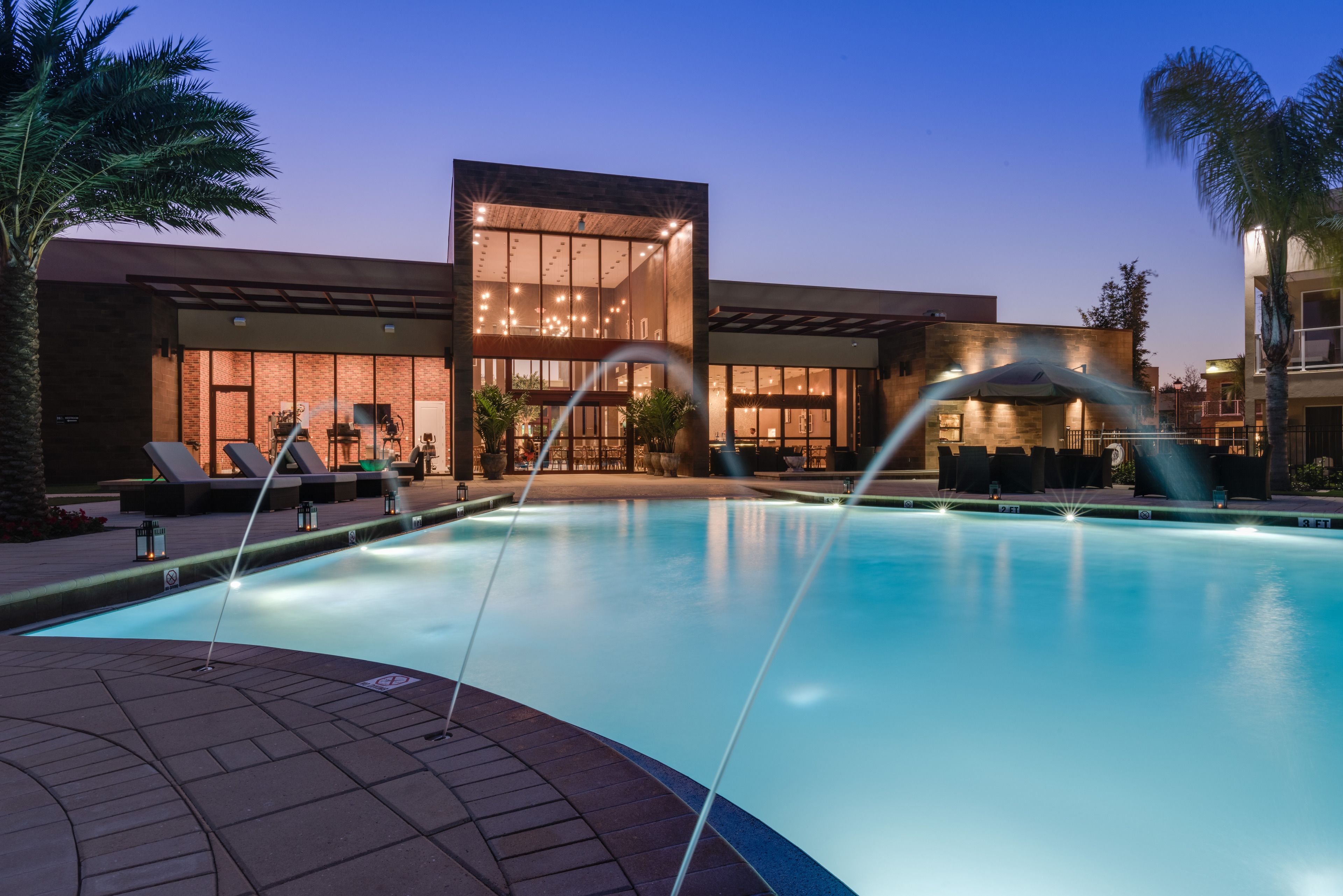 A modern hotel with a swimming pool, lounge chairs, and a well-lit building facade.