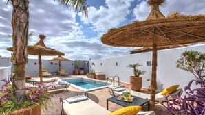 Un área de piscina en la azotea con sillones, sombrillas y plantas en macetas.