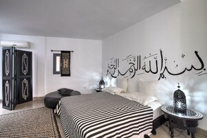 A bedroom with a bed, a nightstand, a decorative wall piece, and a door with a mirror.