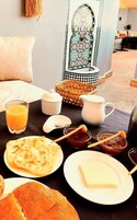 Una colazione preparata con cura: un tavolo apparecchiato per due, con pane, formaggio, marmellata e un bicchiere di succo d'arancia.