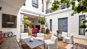 Un patio espacioso con paredes blancas, un cuadro grande y diversas opciones de asiento, incluyendo sillas blancas y un sofá.