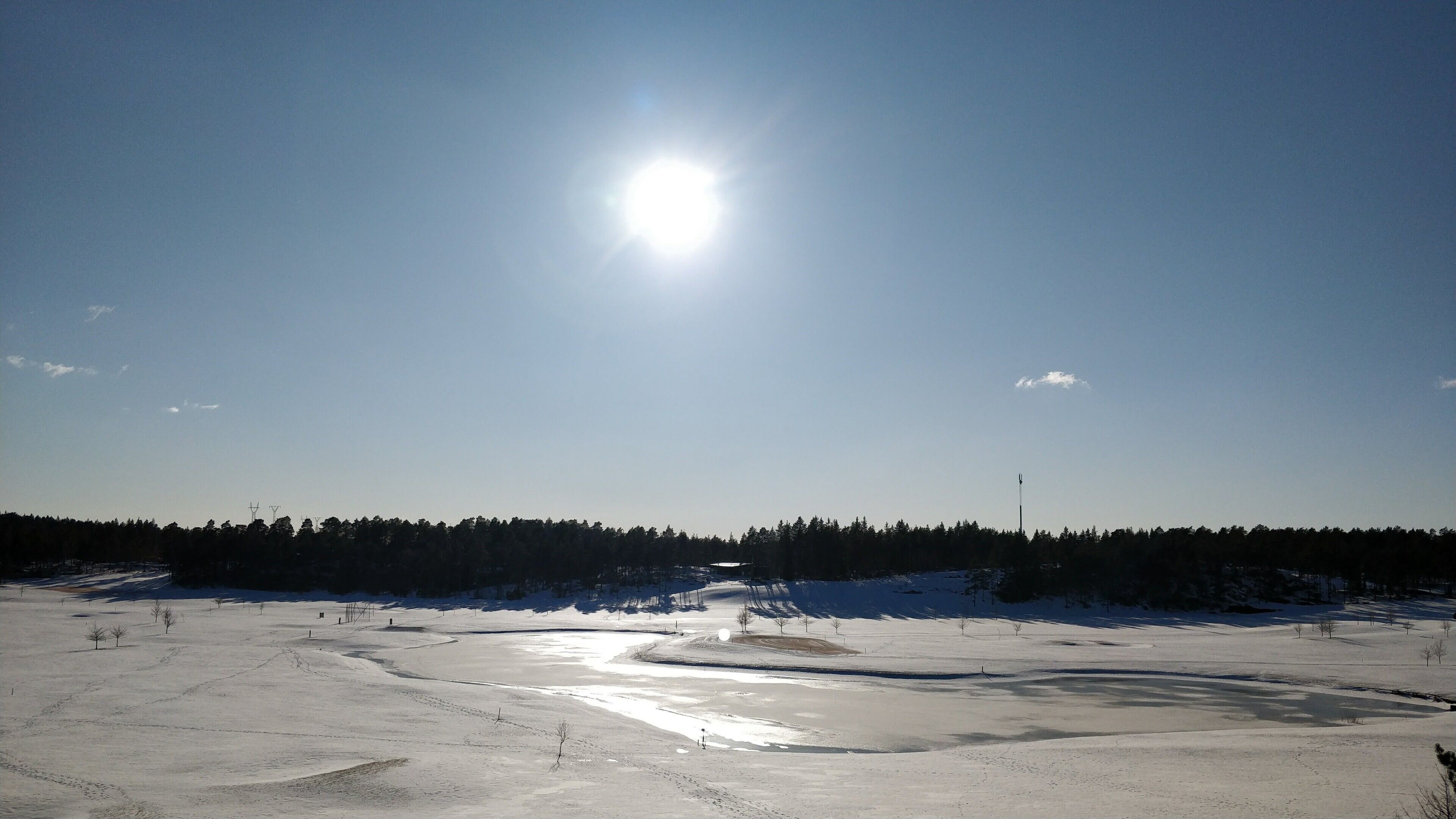 A snow-covered landscape with a clear sky and a bright sun.