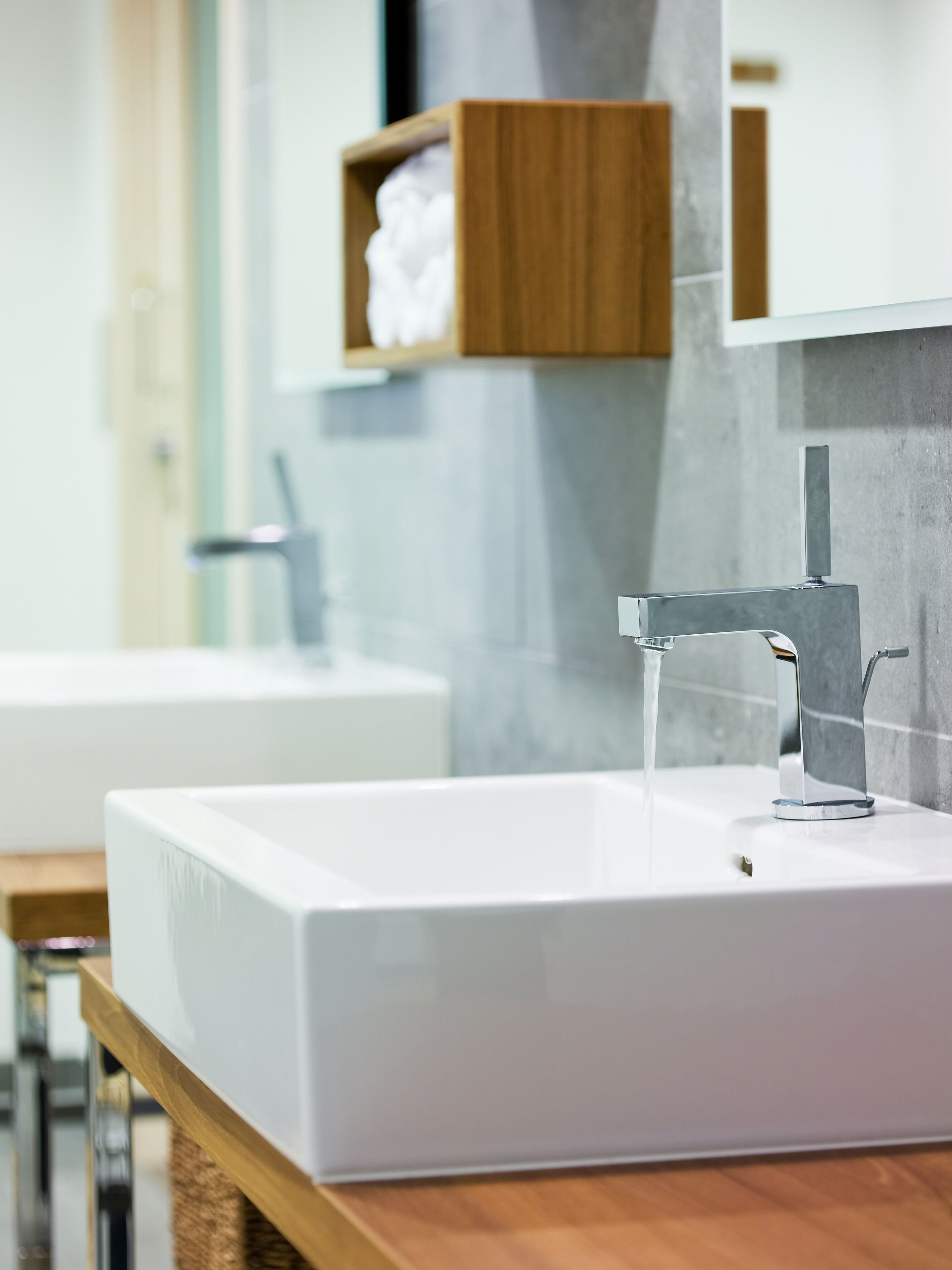 A modern bathroom with a white sink, chrome faucet, and a wooden shelf above it.