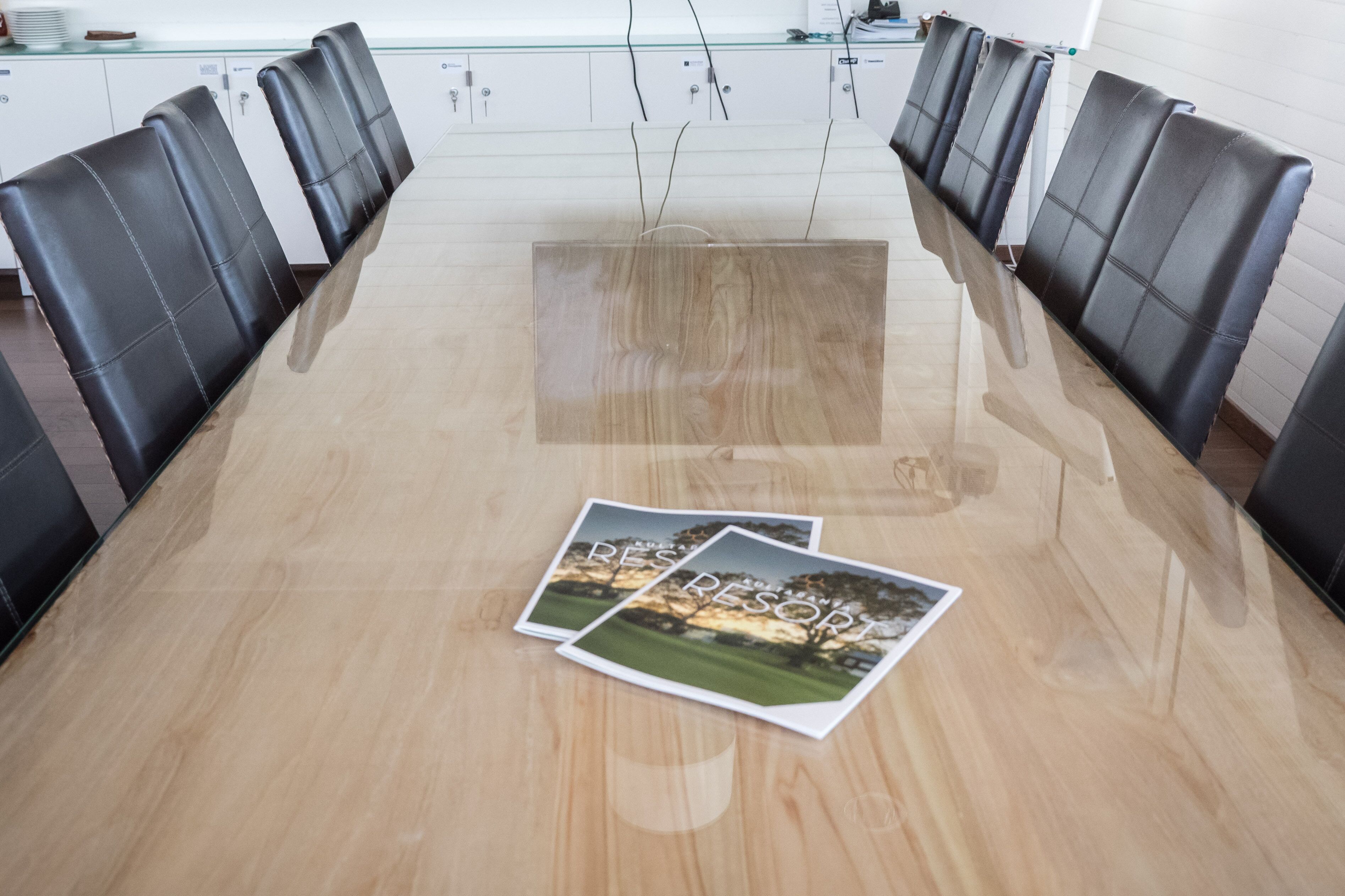 Une salle de conférence avec une longue table, des fauteuils en cuir noir et deux brochures posées sur la table.