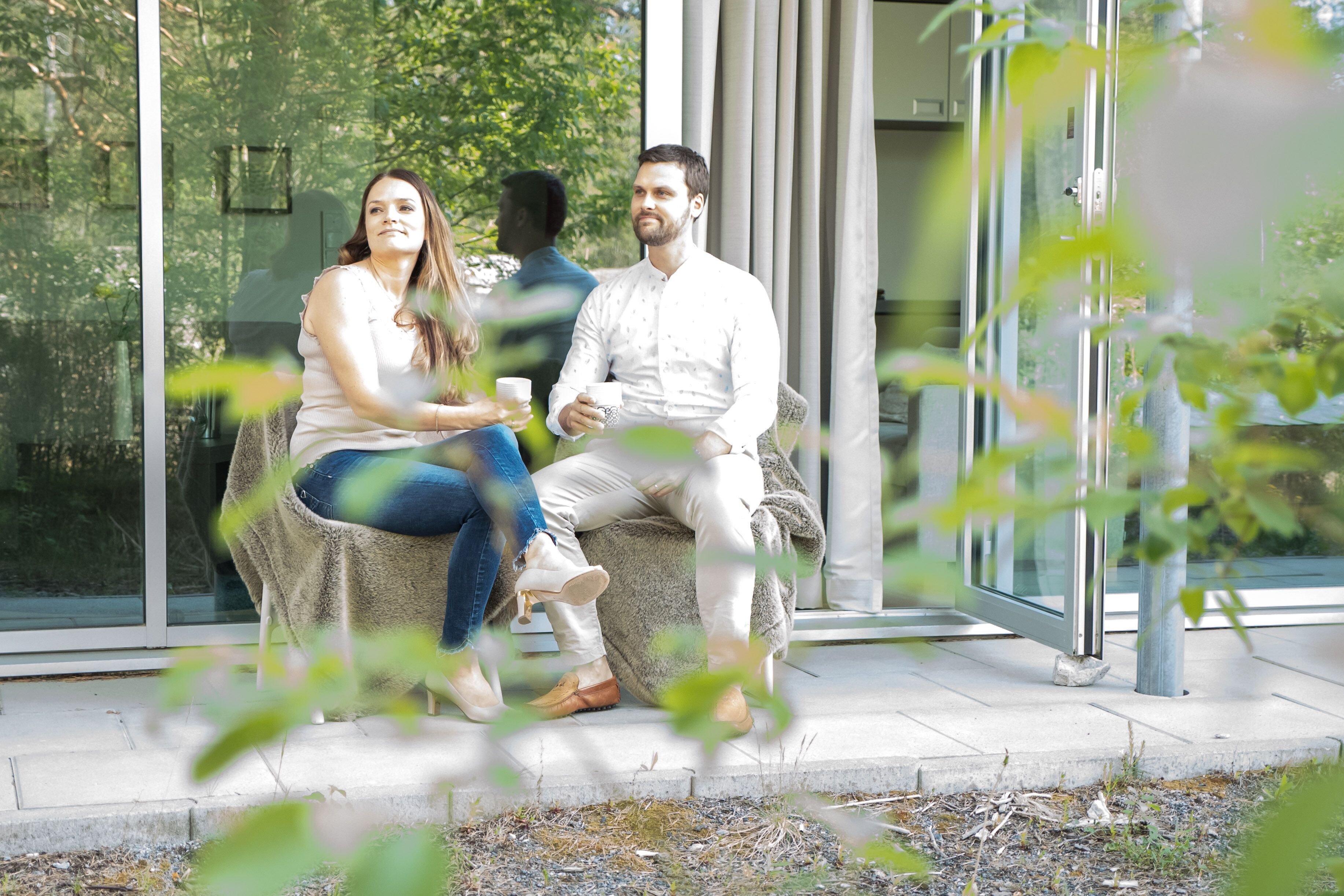 A couple sitting on a bench outside a building with glass walls, a clear view of trees, and a modern architectural style.