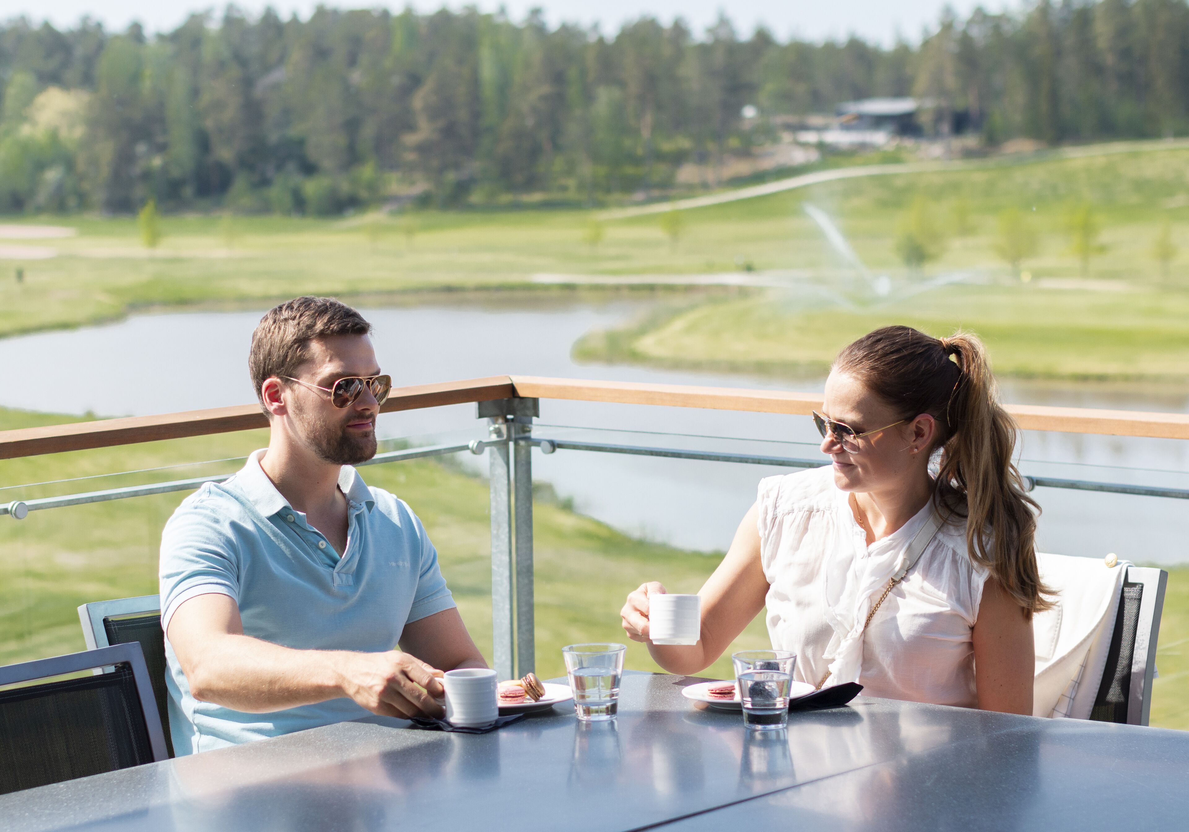 Una pareja cenando en una mesa con vistas a un lago y un bosque.
