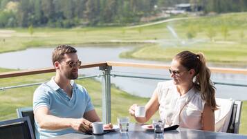 Una pareja cenando en una mesa con vistas a un lago y un bosque.