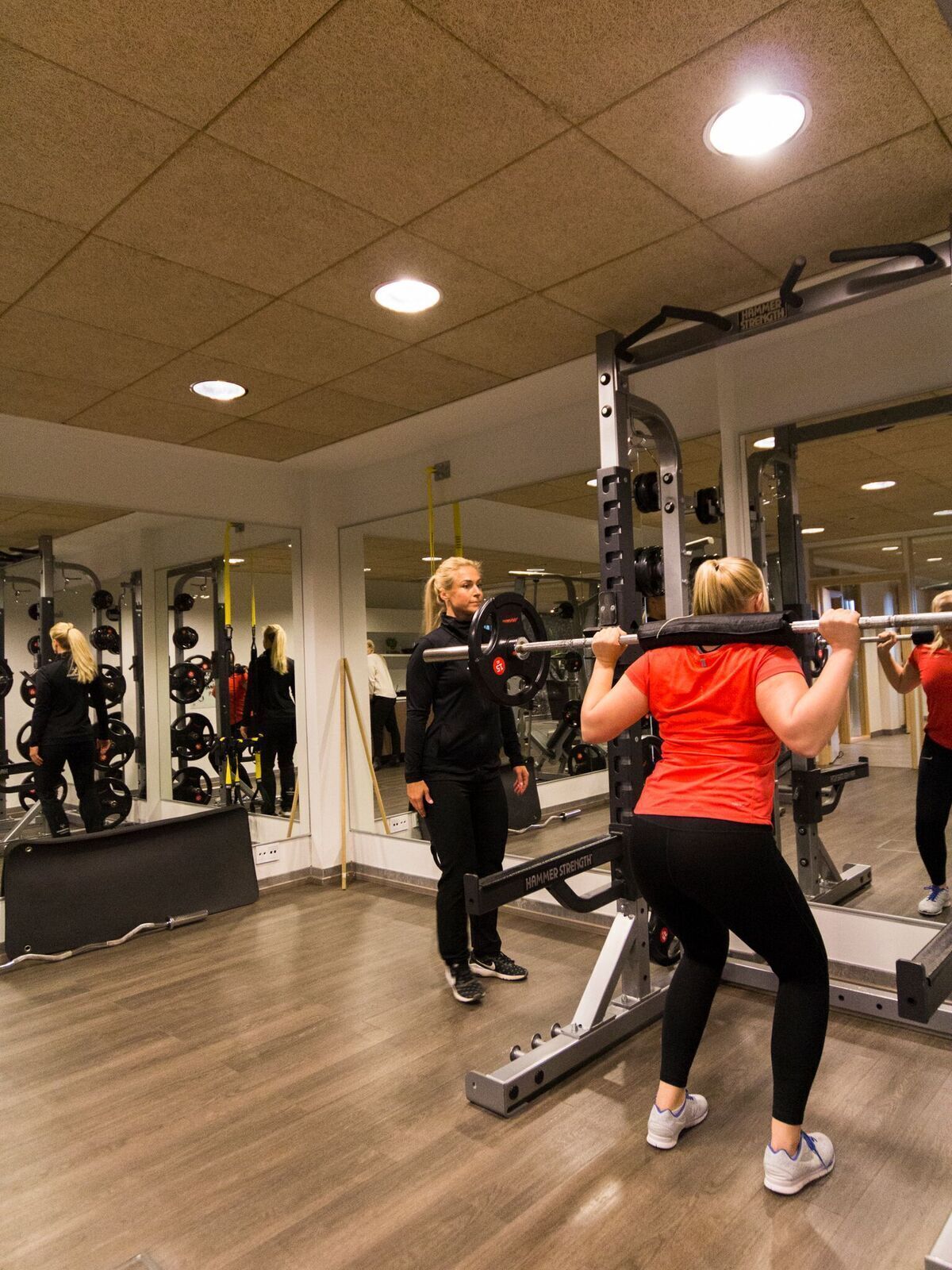 A gym with weightlifting equipment, mirrors, and a wooden floor.