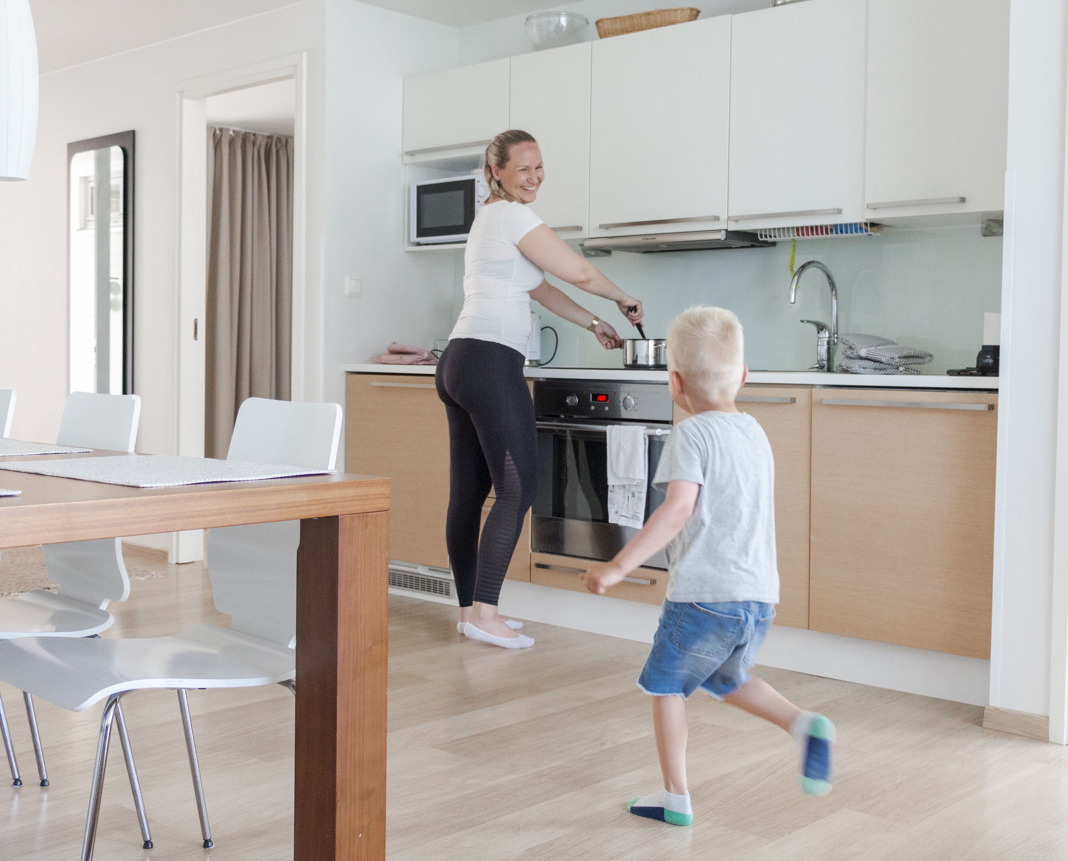 A modern kitchen with white cabinets, a microwave, and a stove. There is a dining table with chairs and a person cooking.