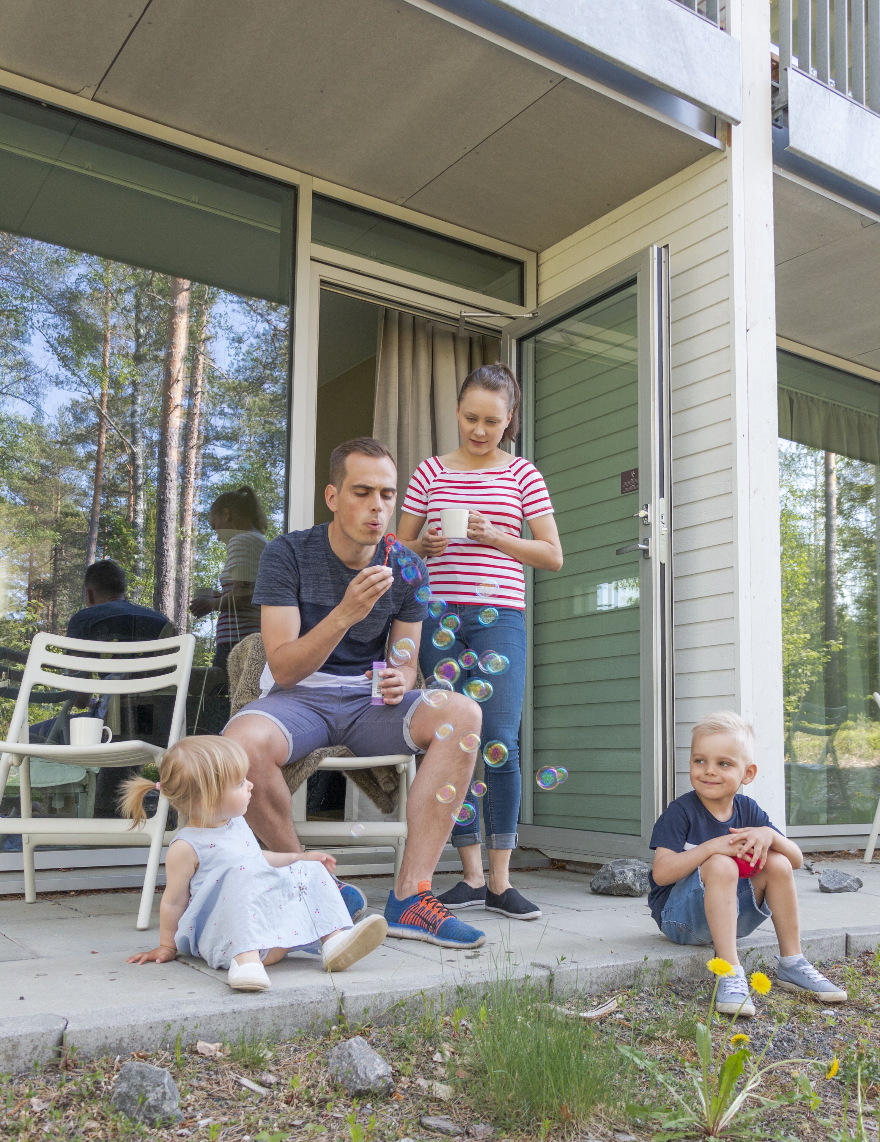 A family sitting on a porch with a glass door leading to a green interior.
