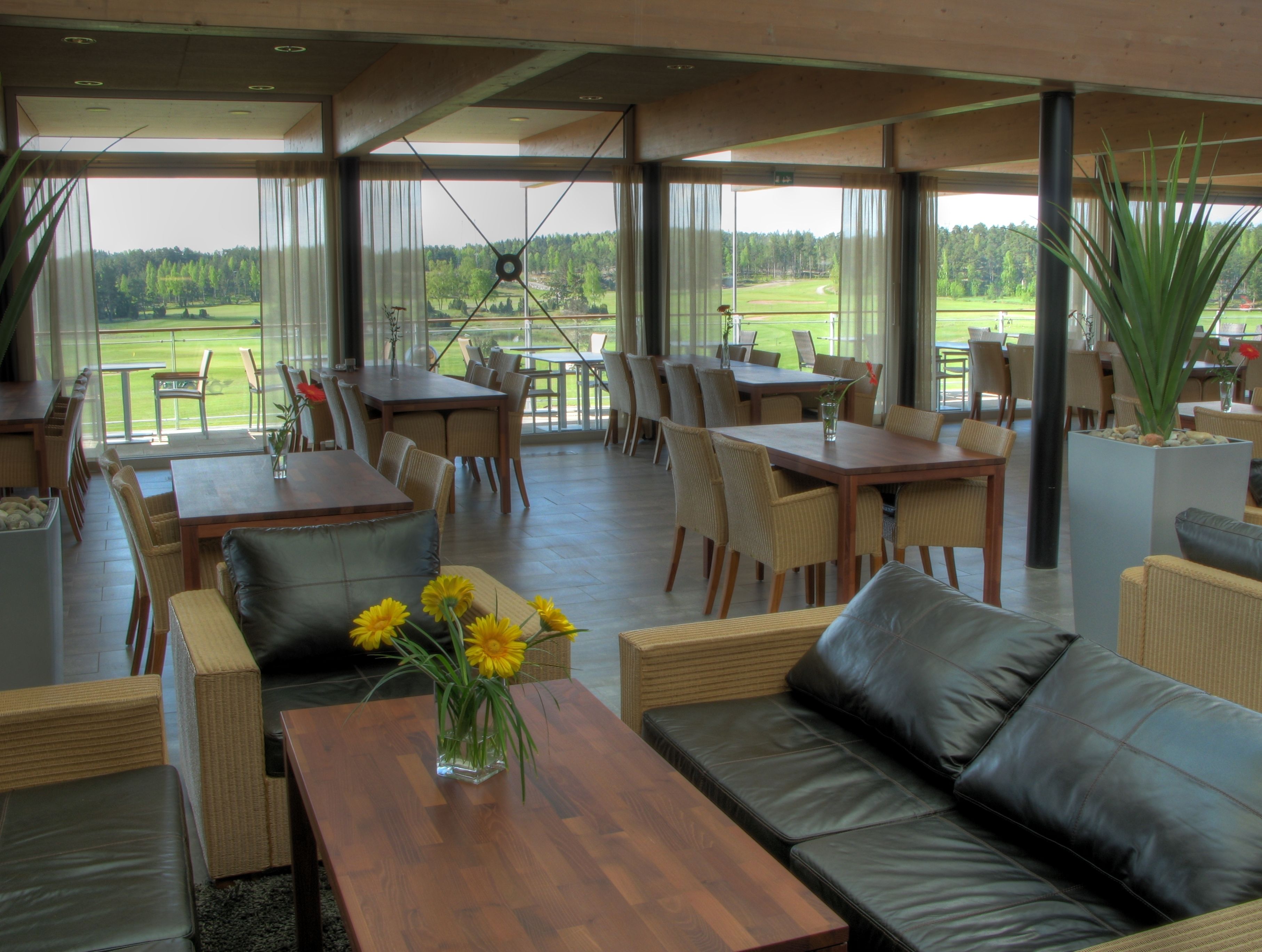 A spacious indoor area with multiple seating arrangements, including sofas and tables, and large windows offering views of a golf course.